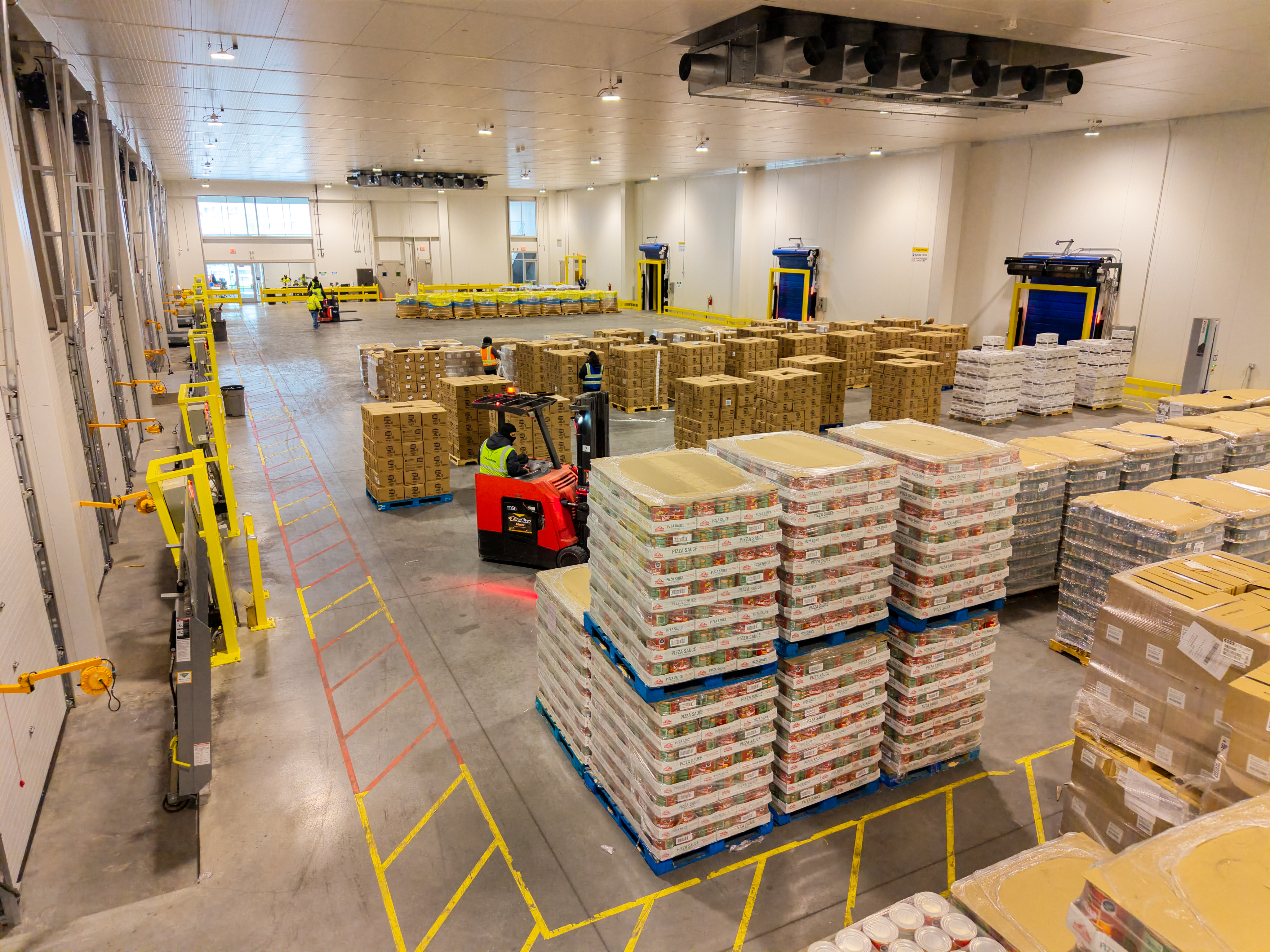 Large refrigerated warehouse operation with staged inventory, dock doors, and active movement.