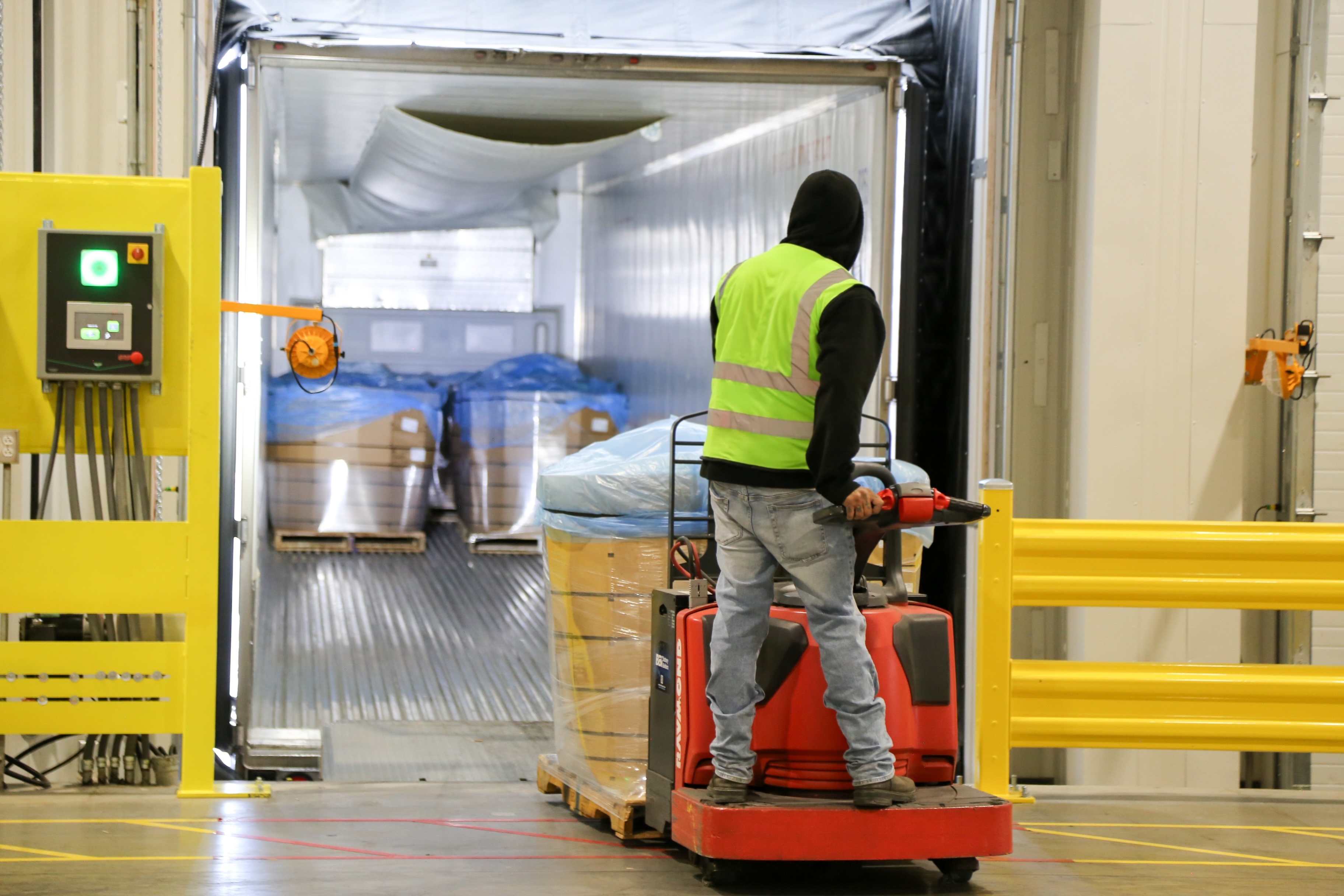 Operator moving palletized refrigerated product into a trailer at a controlled dock.