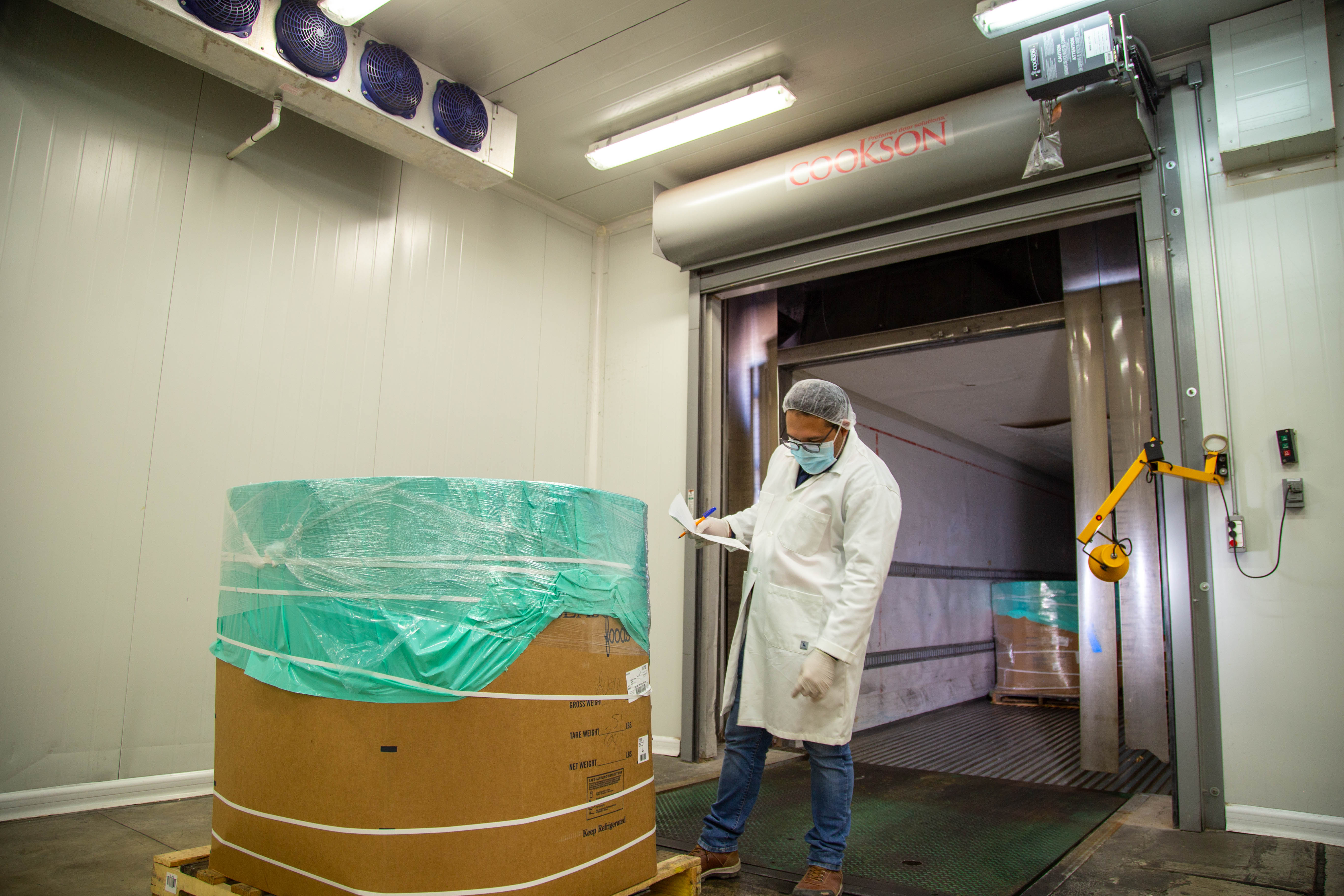 Inspector reviewing release documentation beside refrigerated product and dock equipment.
